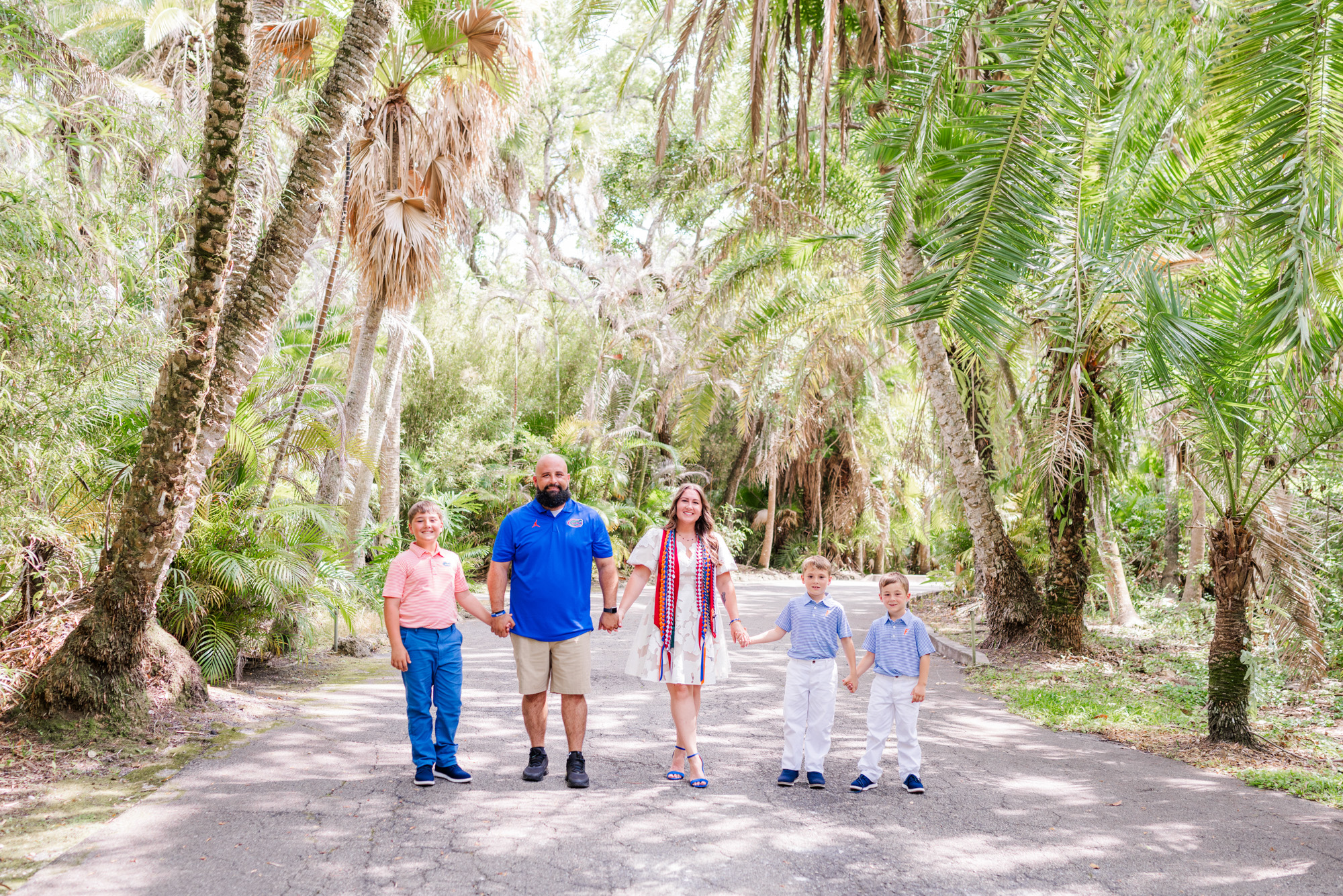 Family walking together along a tree-lined road at the Florida Tech Botanical Gardens.