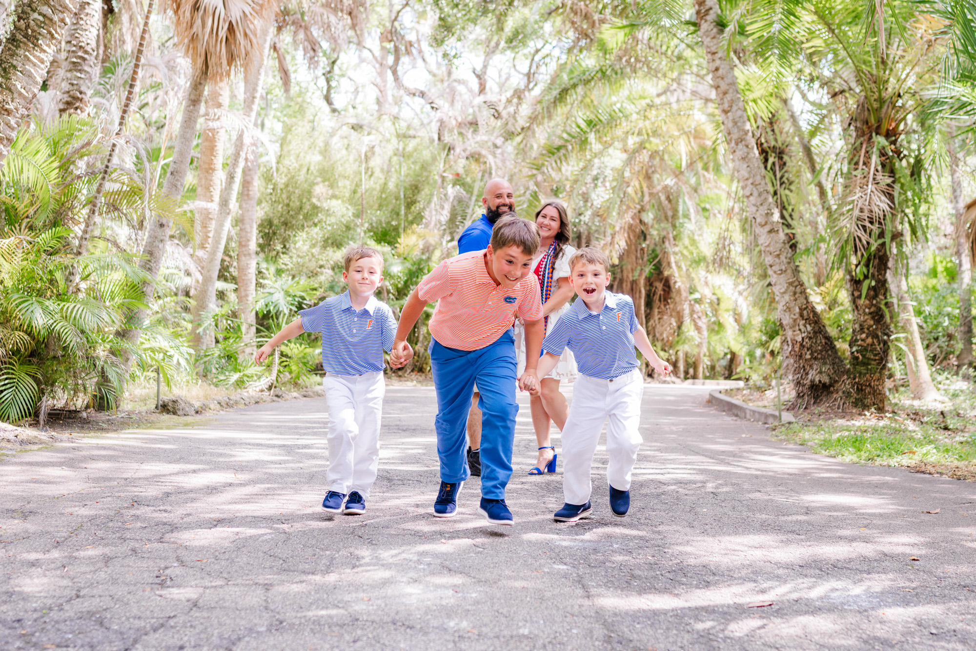 Family playfully running toward the camera along a shaded garden road.