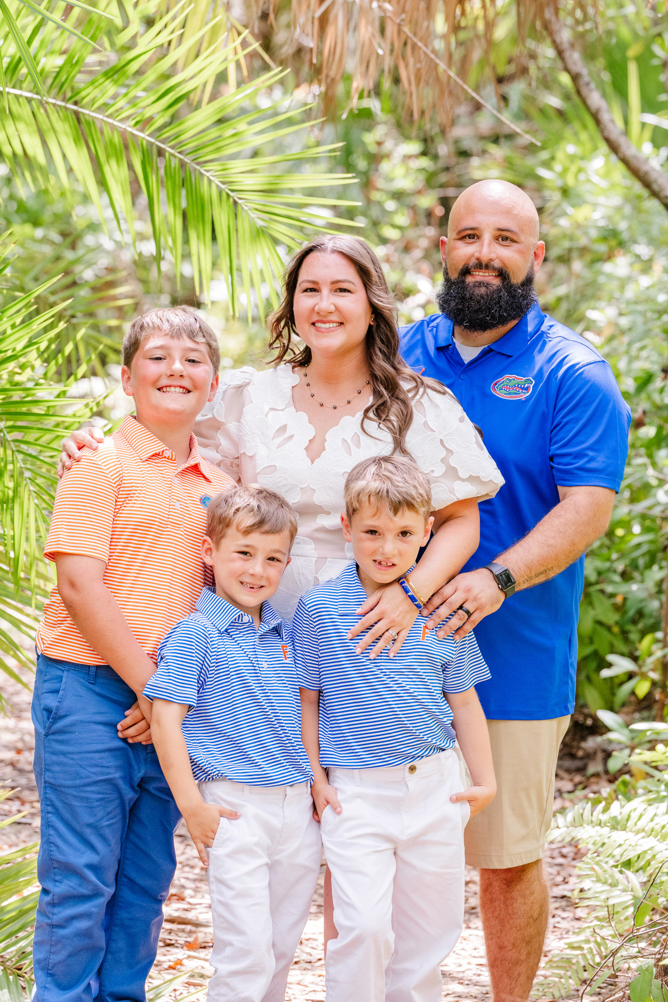 Family of five smiling together beneath palm trees and lush greenery.