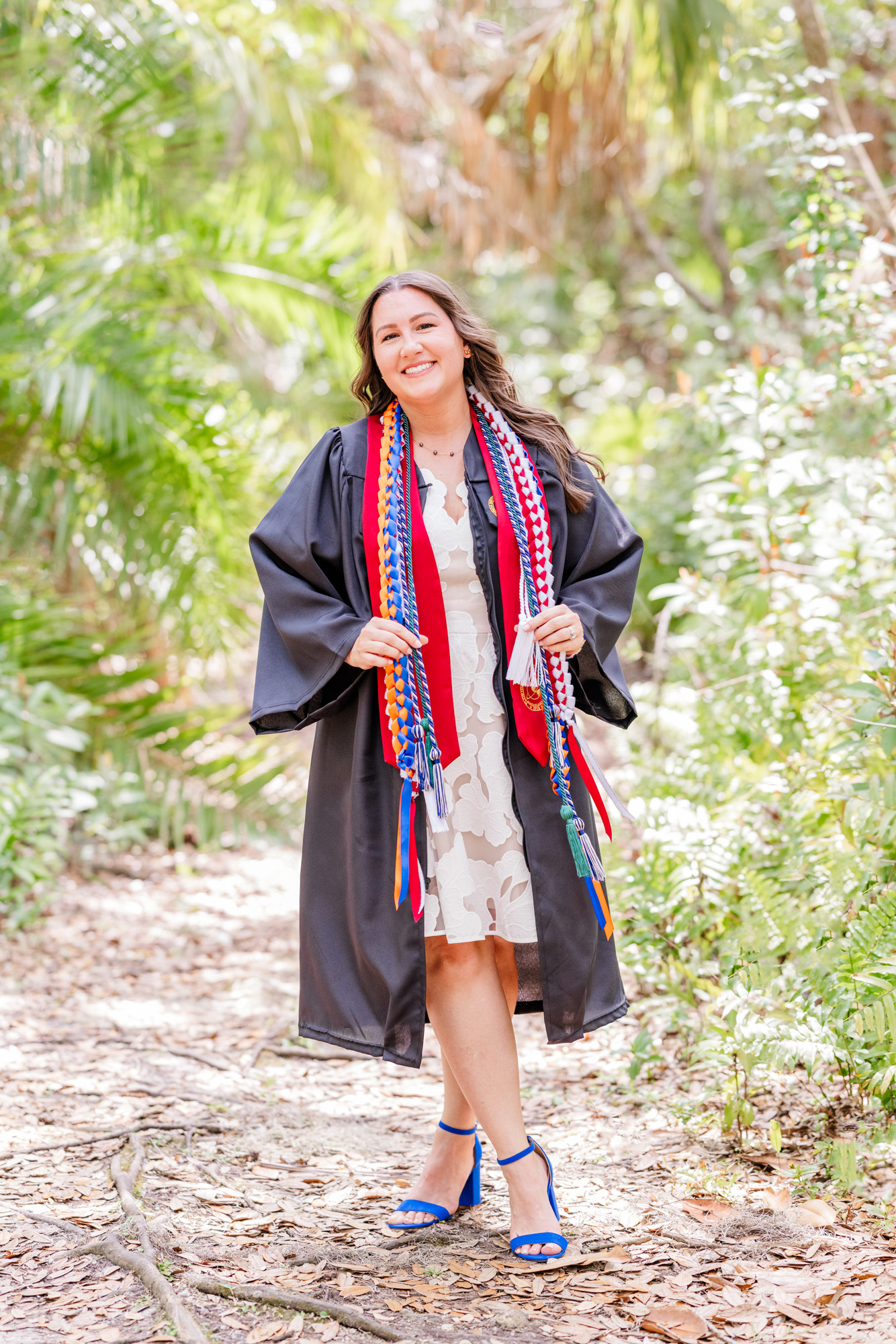 Graduate standing confidently in her cap and gown on a tropical garden path.