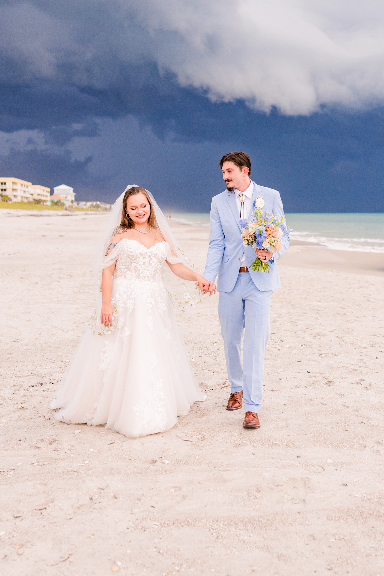 Bride and groom walking down beach with groom holding the bouquet