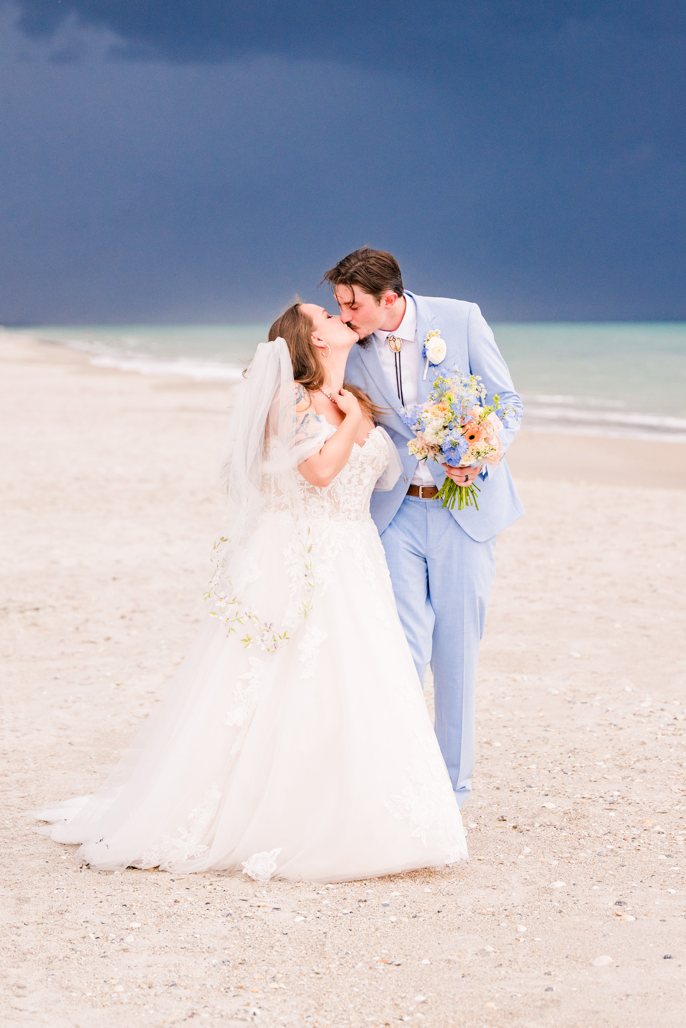 Couple kissing on beach after getting married with a stormy sky