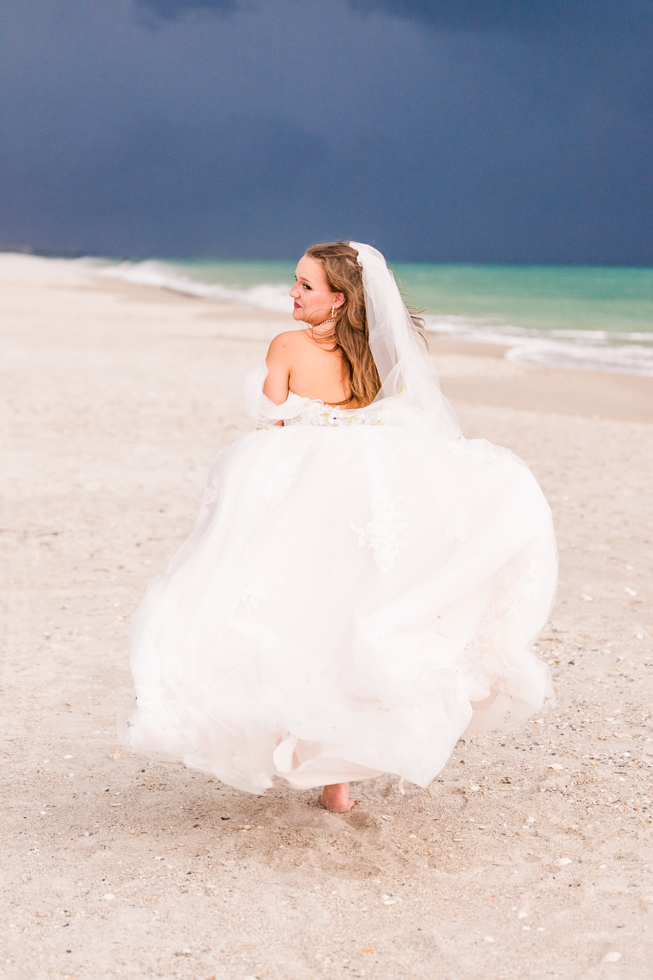 Bride looking over shoulder while running down beach during a stormy sky