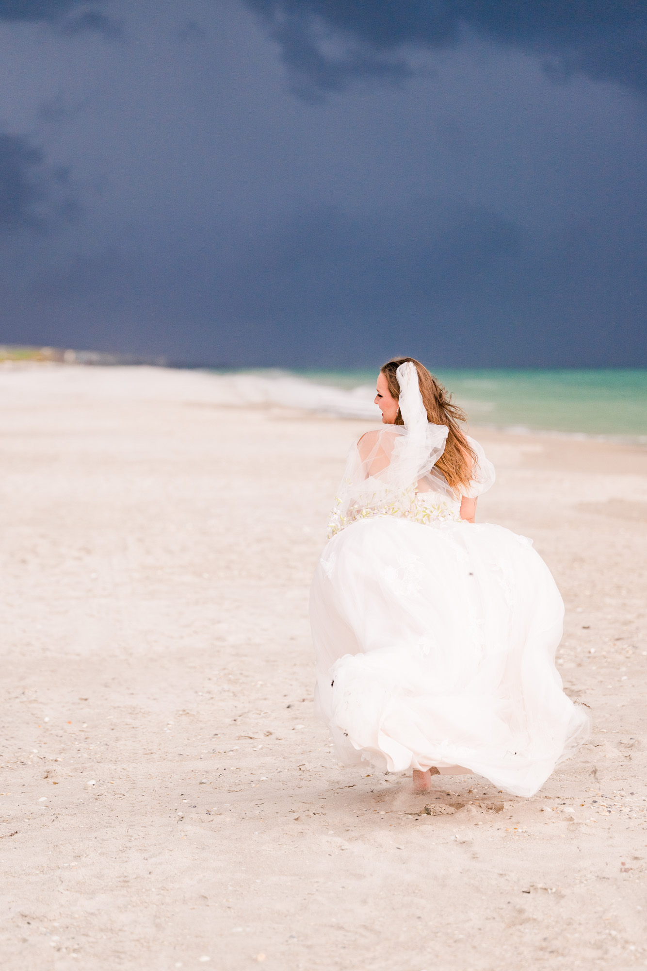 Bride in flowing dress running down beach with a very stormy sky