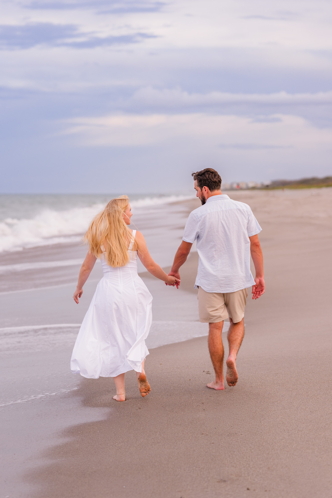 couple walking with their backs to the camera down Melbourne Beach during their engagement session
