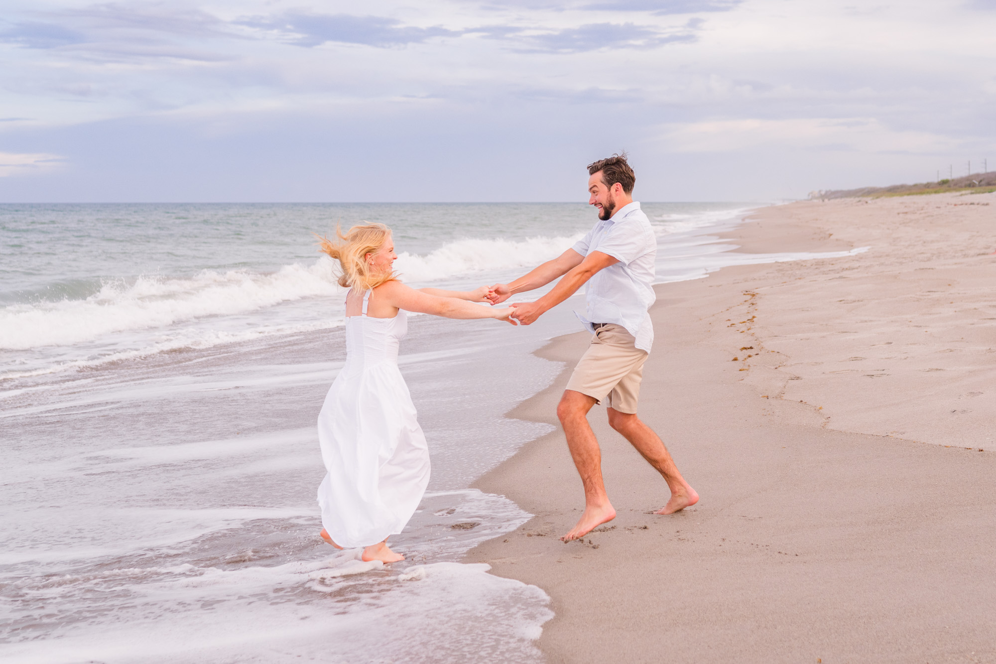 couple holding hands and spinning on Melbourne Beach during their engagement session