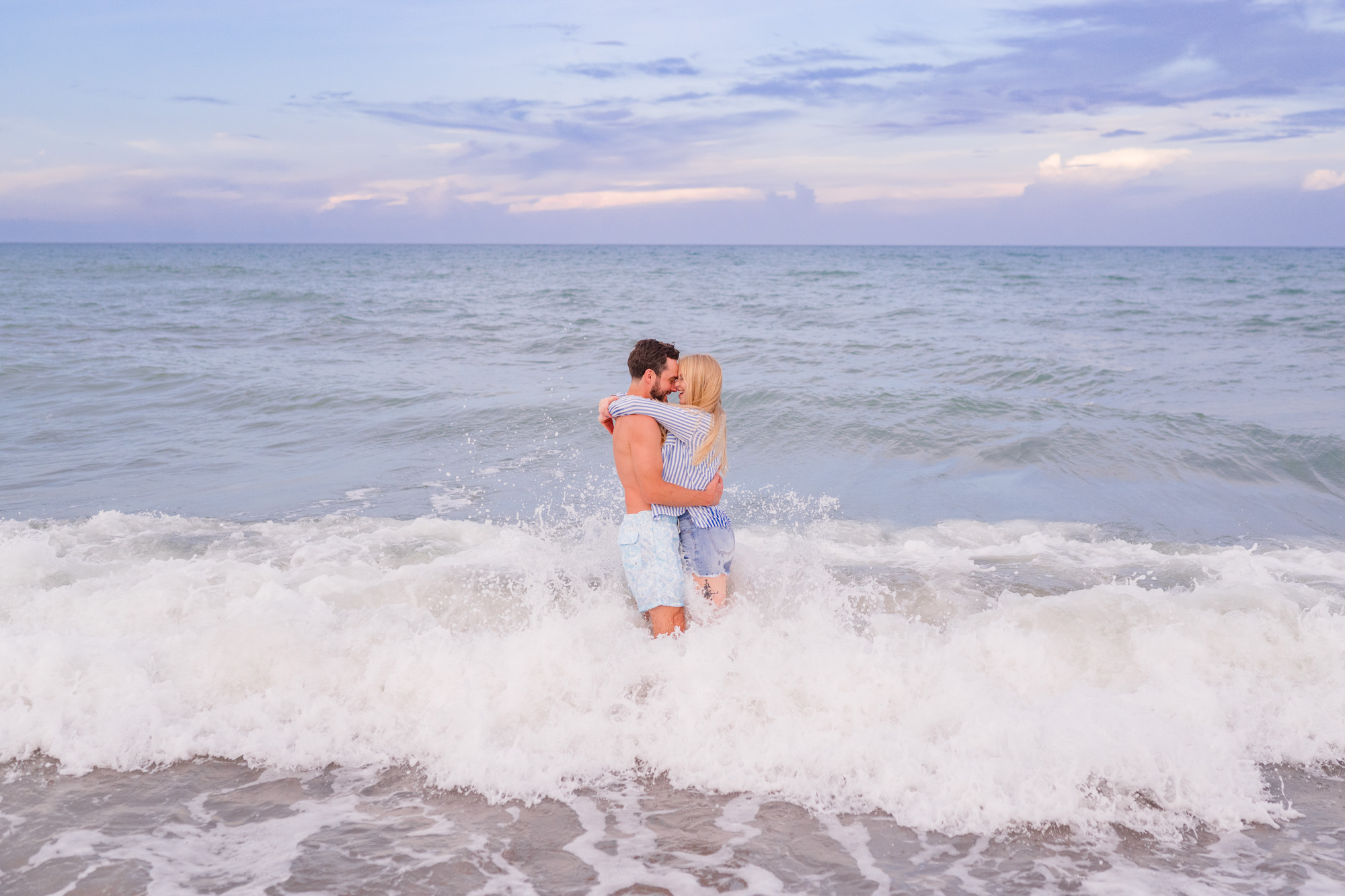 Couple hugging in the surf while a wave splashed over them