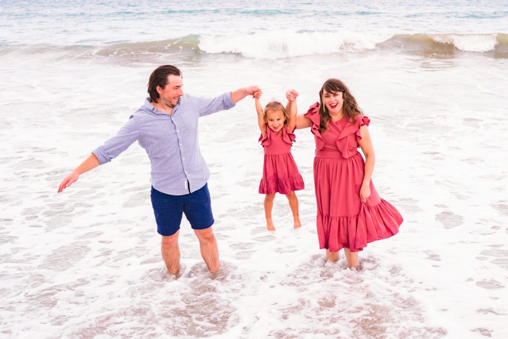 couple swinging their daughter in a pink dress in the water