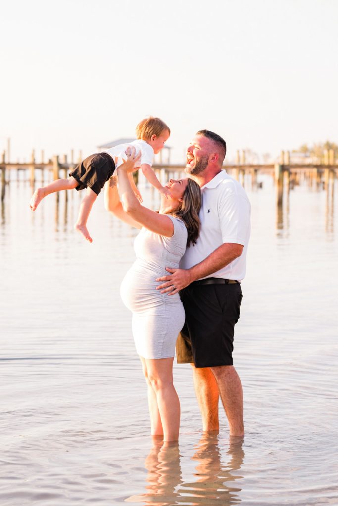 family standing in the river during sunset holding small child in the air
