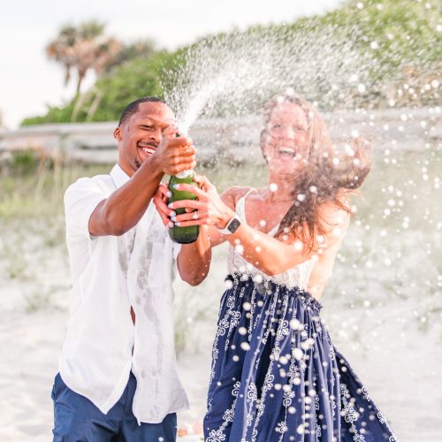 Couple popping champagne bottle on the beach after she said yes to marrying him