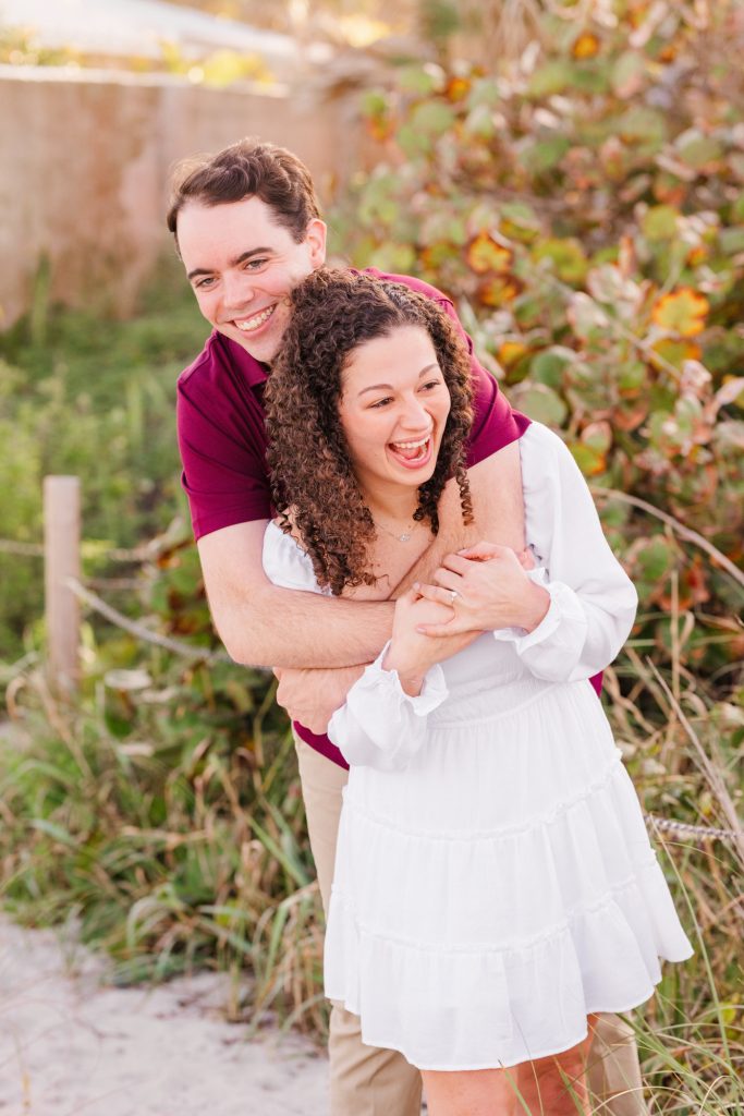 Man hugging woman who is laughing during engagement session on the beach
