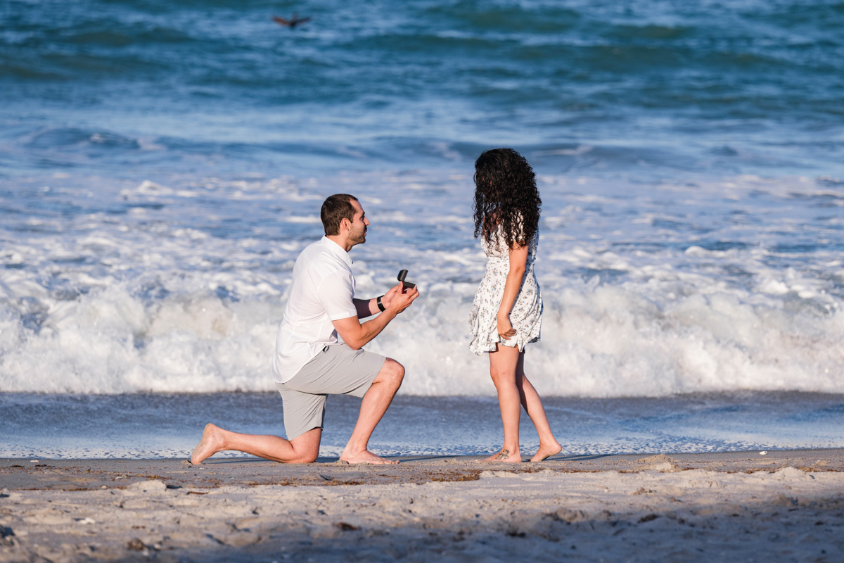A sunny day at the beach with a man near the ocean proposing to a woman on Melbourne Beach