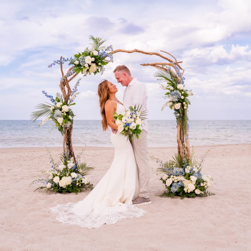 Wide shot of bride and groom under the arch after getting married on Melbourne Beach