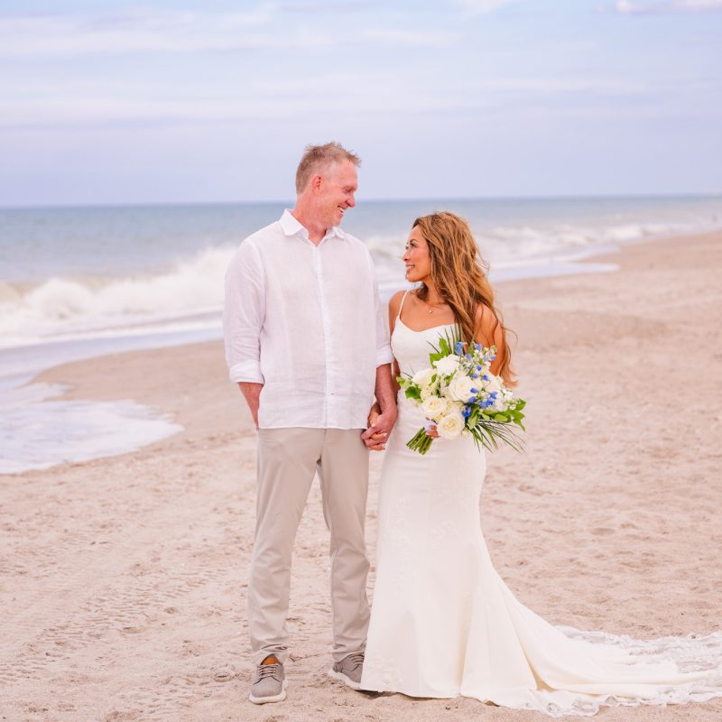 Bride and groom walking down the beach looking at each other
