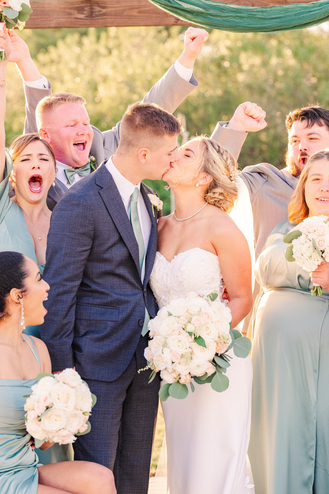 Wedding couple kissing while the wedding party cheers