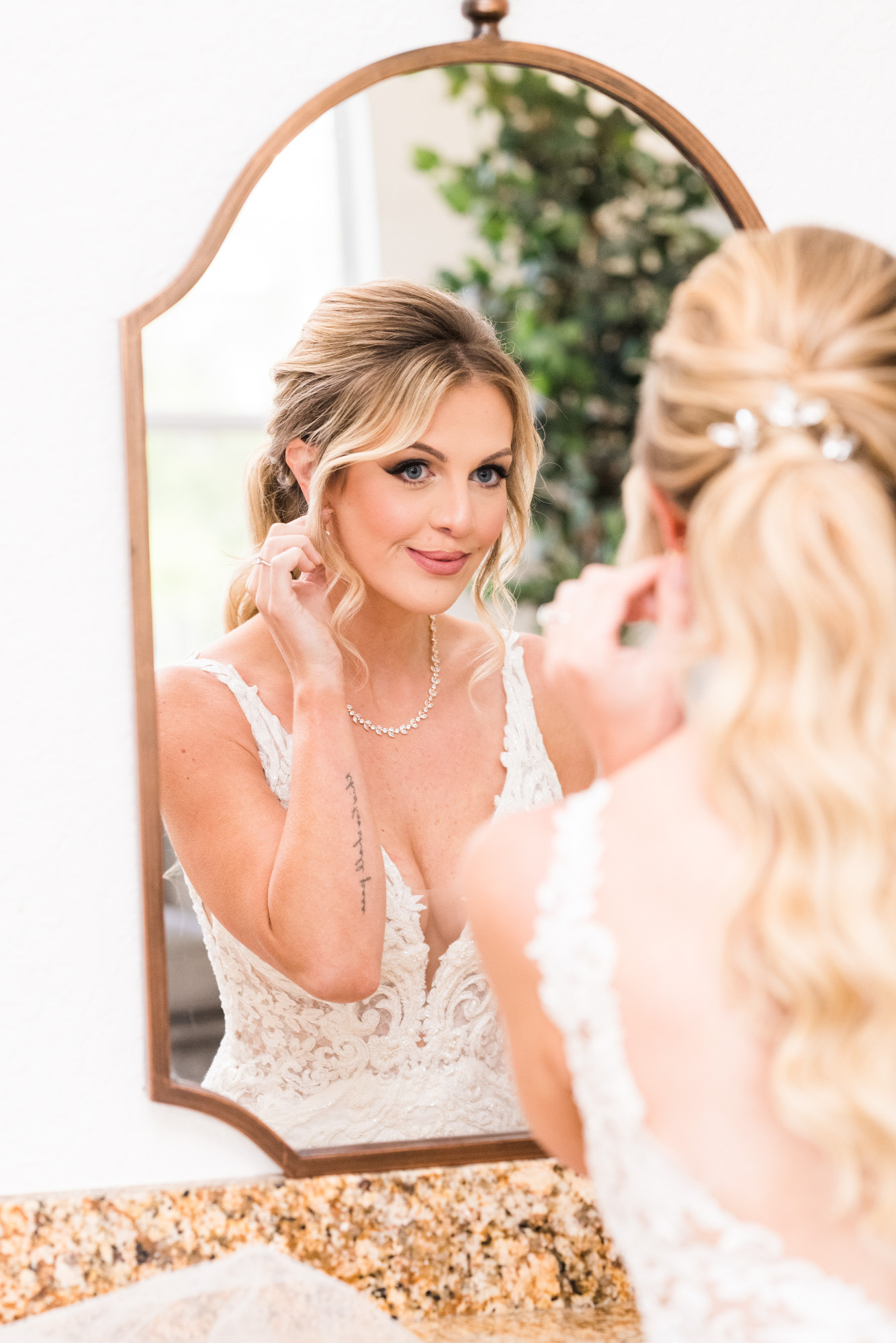 Bride adjusting ear ring while looking in mirror at her wedding