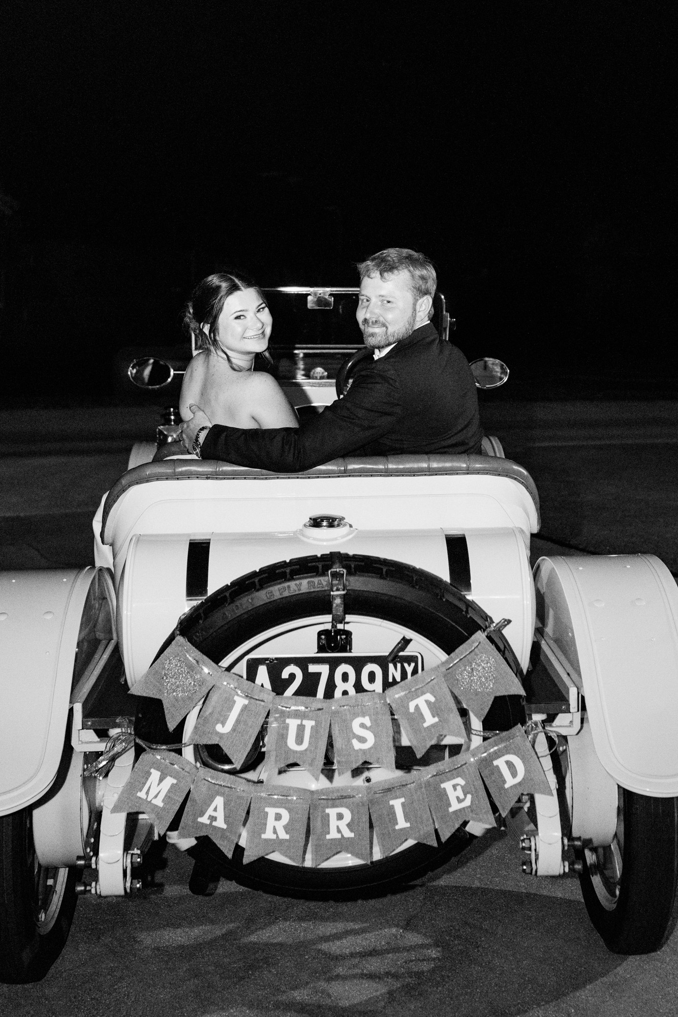 Black and white picture of bride and groom in antique getaway car