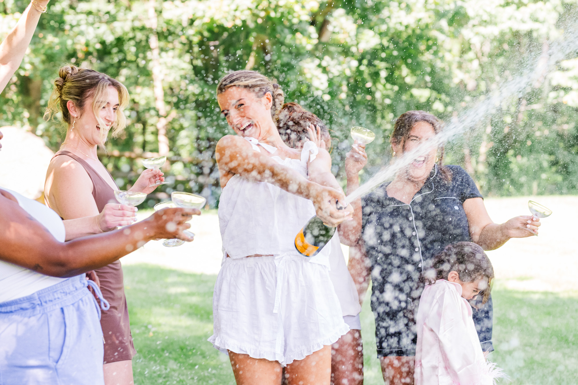 Bride popping a bottle of champagne with her wedding party before the ceremony