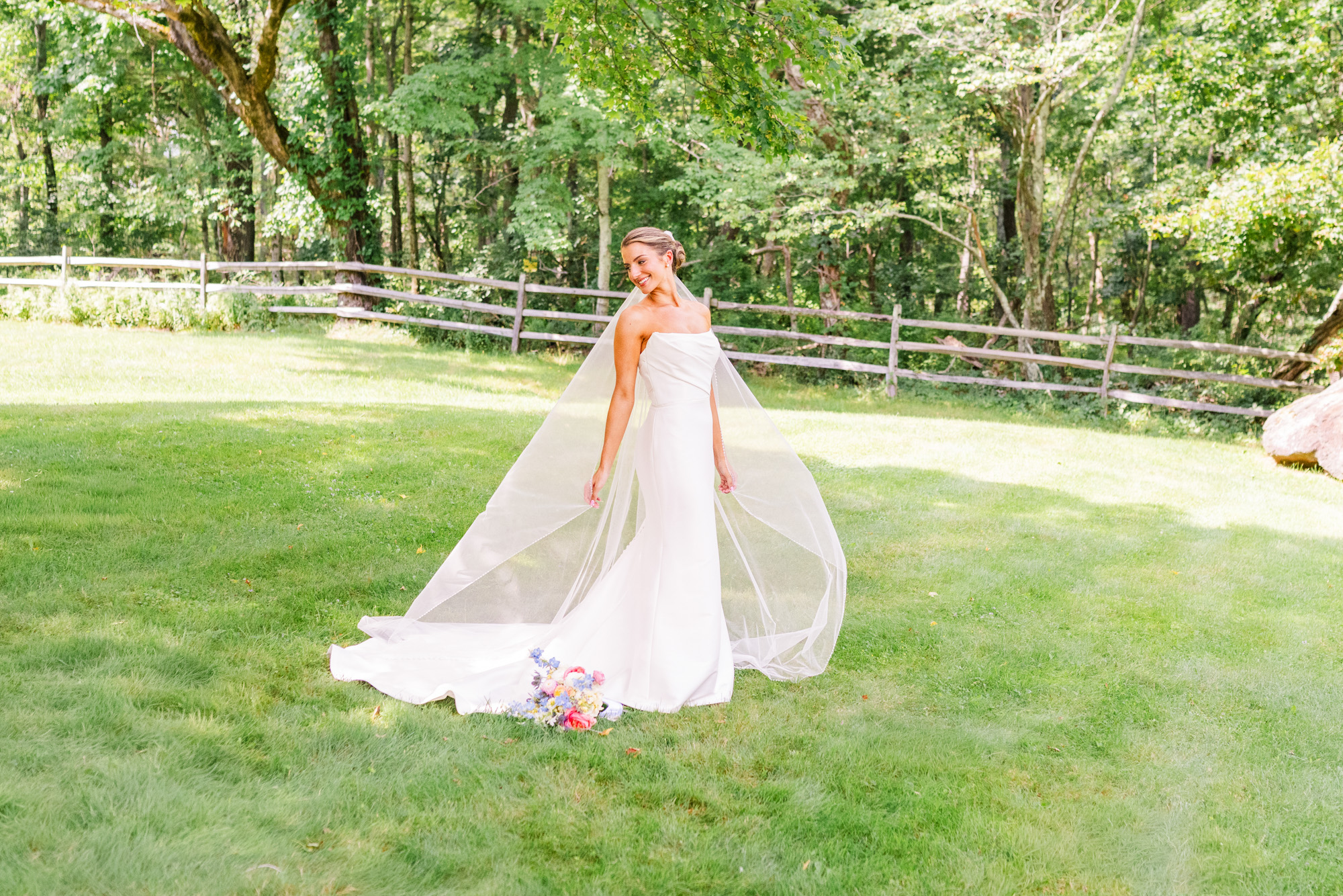 Bride standing on the lawn with her long veil flowing behind her