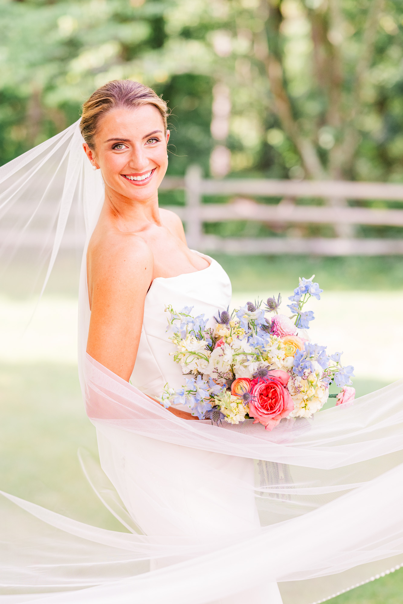 Bride wrapped in her veil holding a colorful summer wedding bouquet