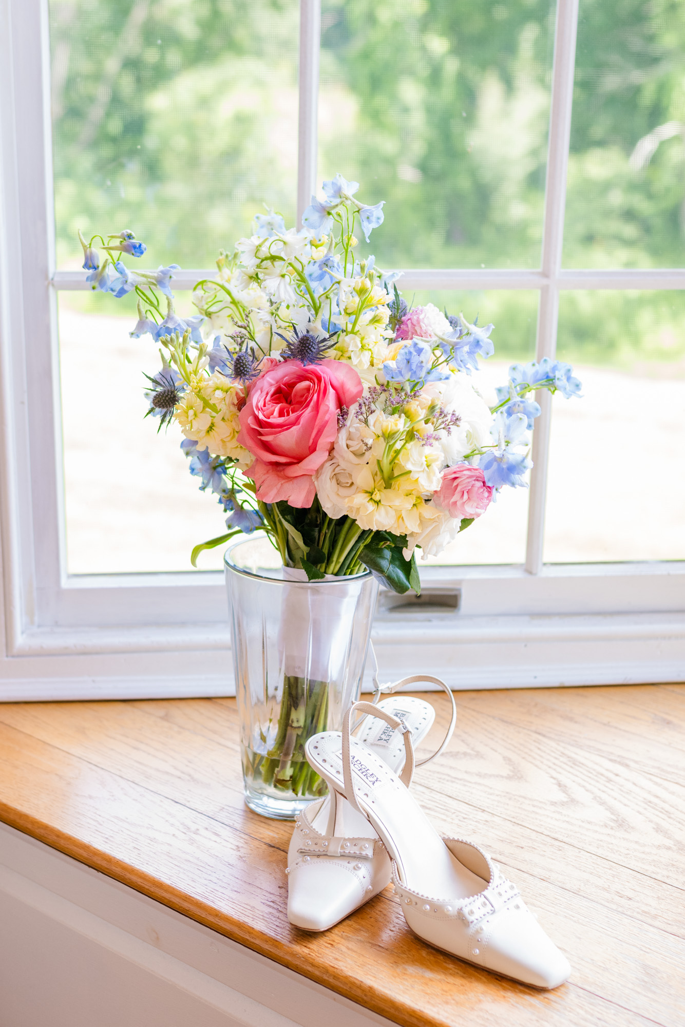 Colorful wedding bouquet and white bridal shoes beside a window in Pawling, New York