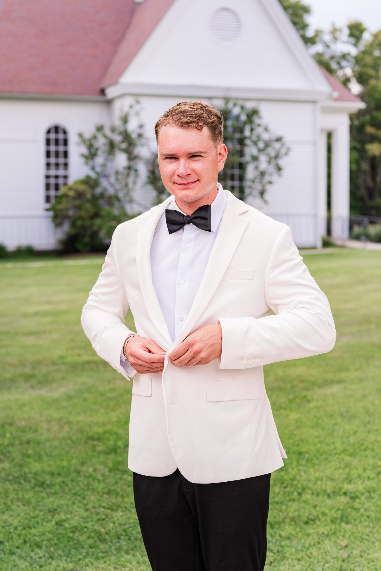 Groom portrait buttoning his white dinner jacket