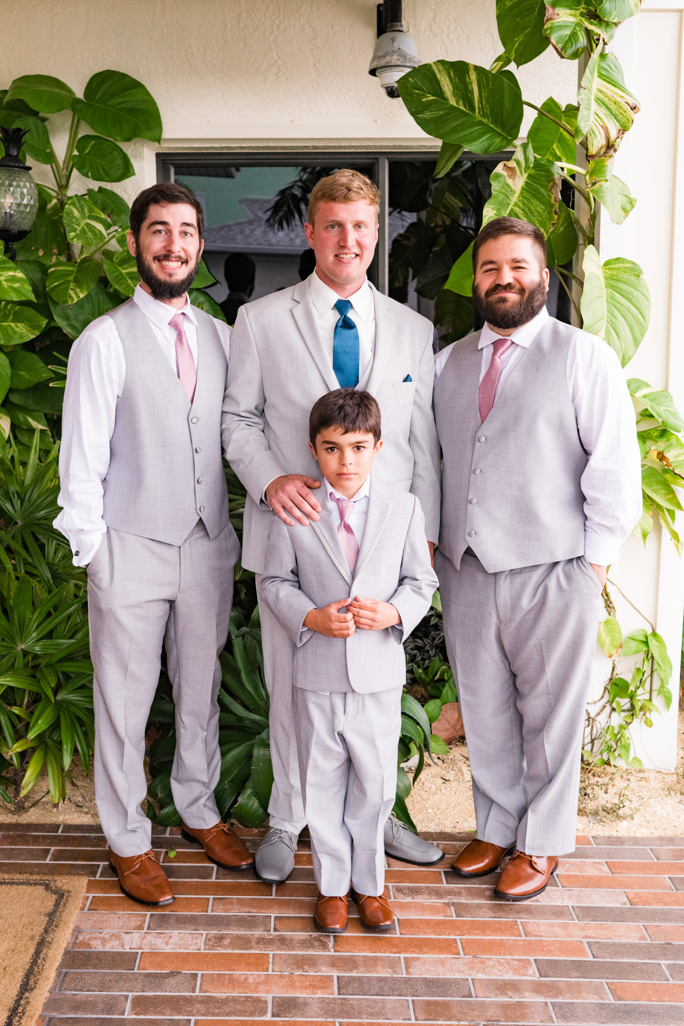 Groom with his wedding party in light gray suits standing beside tropical greenery before the
