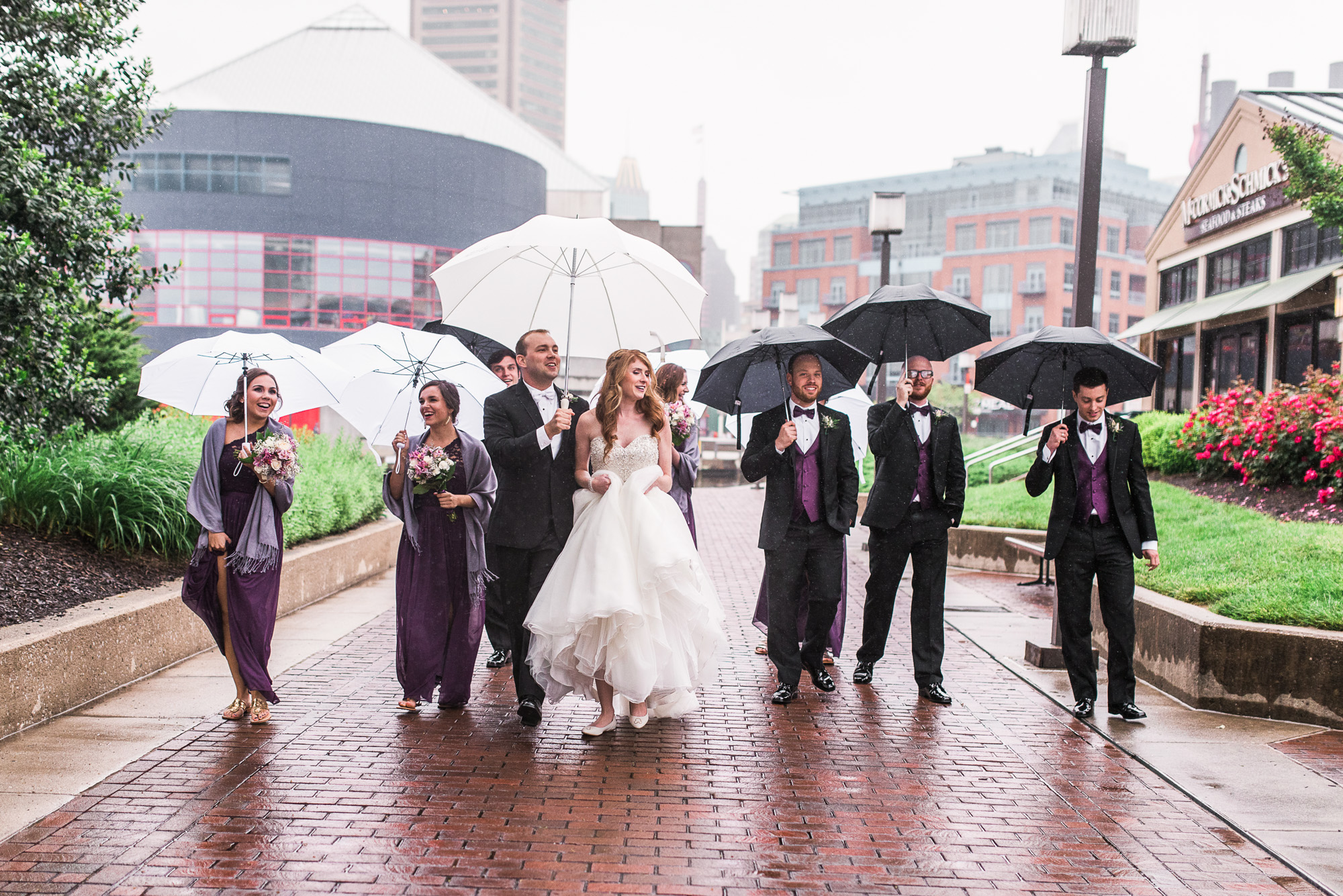 Wedding party walking in the rain with umbrellas during an urban wedding day in Baltimore.