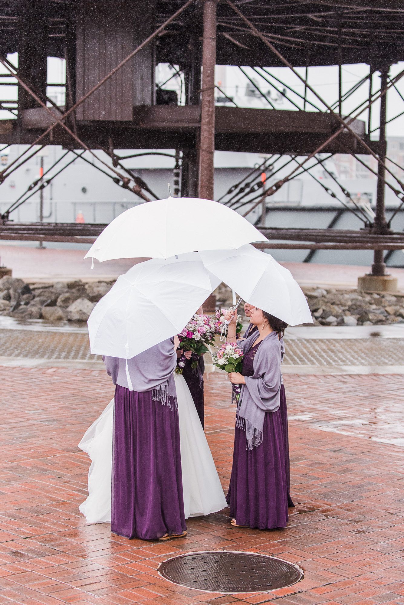 Bridesmaids holding white umbrellas during rainy wedding portraits.
