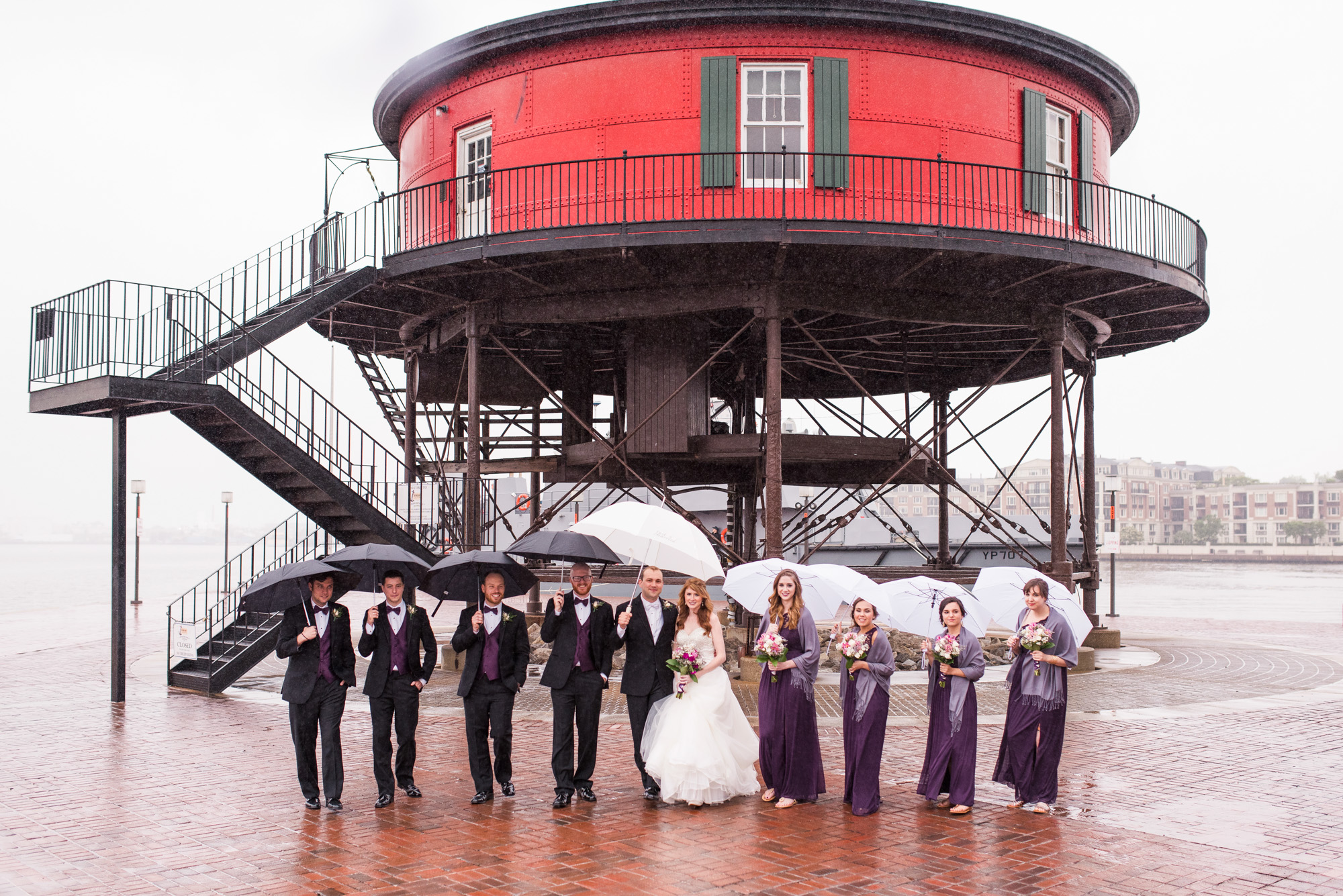 Wedding party posing with umbrellas in the rain at an industrial waterfront location in Baltimore.