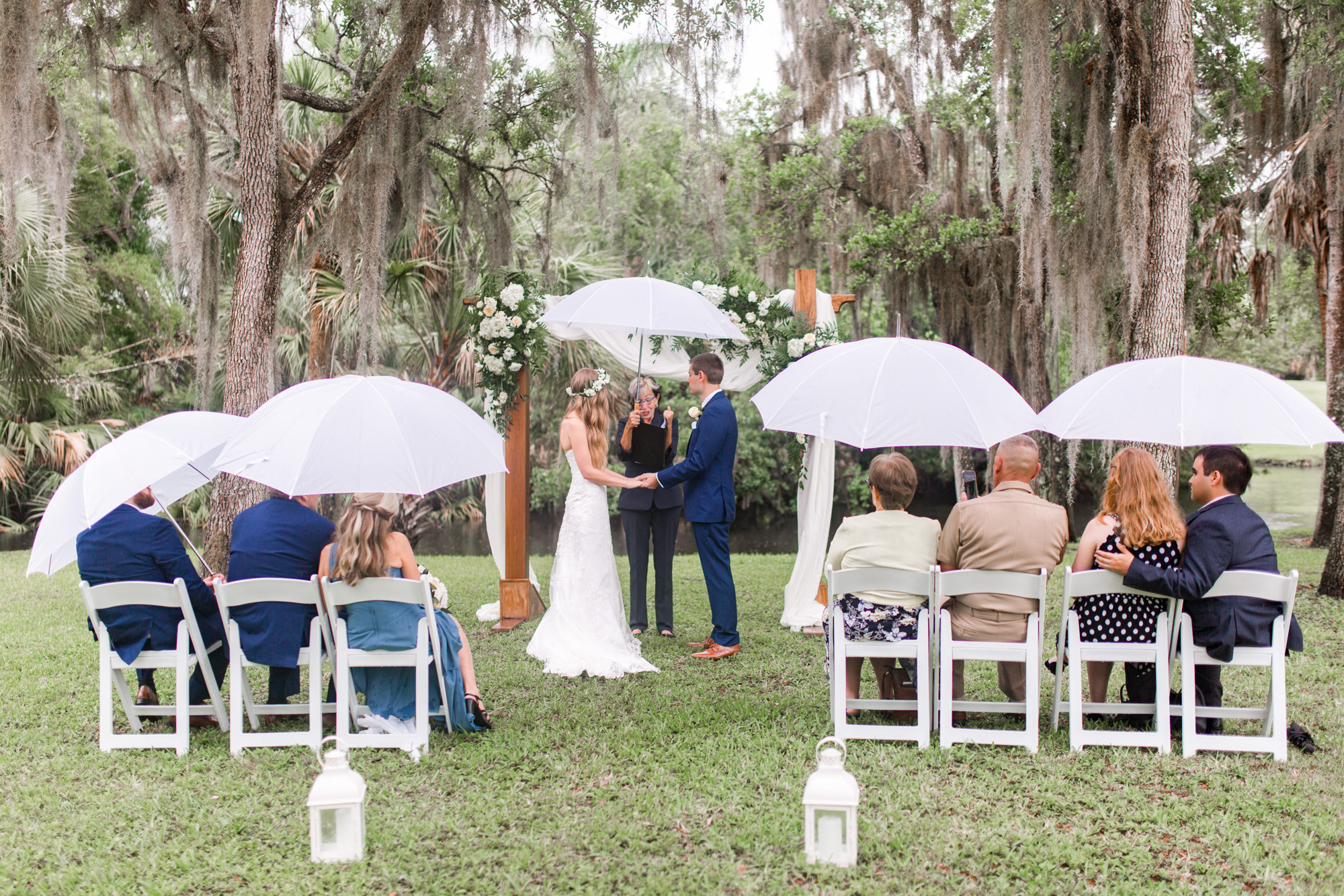 Outdoor wedding ceremony continuing in light rain with guests holding white umbrellas at Up the Creek Farms.