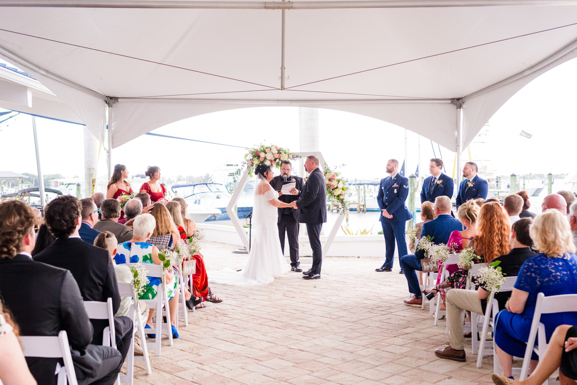 Covered waterfront wedding ceremony beneath a tent during uncertain Florida weather at the Eau Gallie Yacht Club.