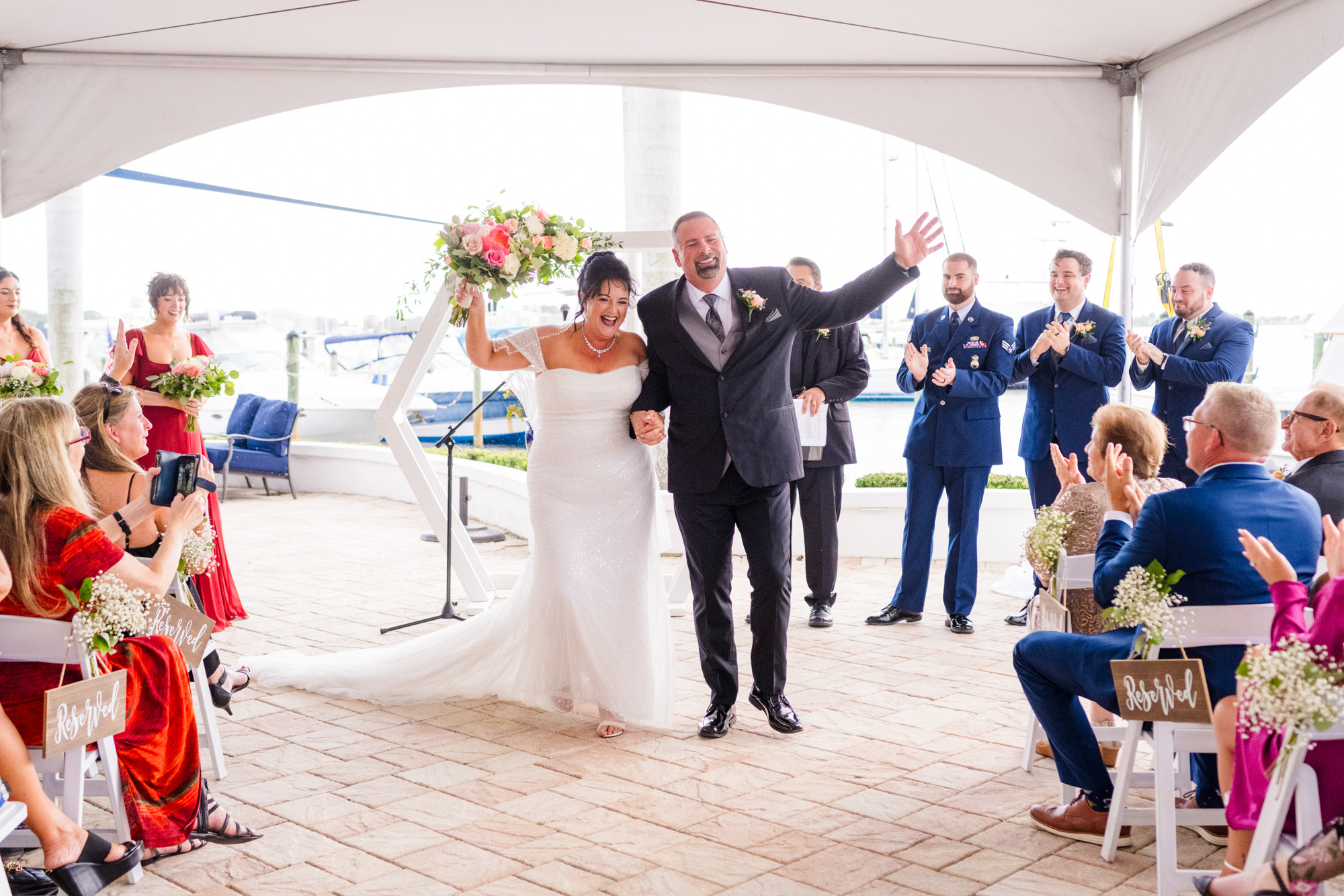 Newlyweds celebrating as they walk back down the aisle after a covered waterfront ceremony.