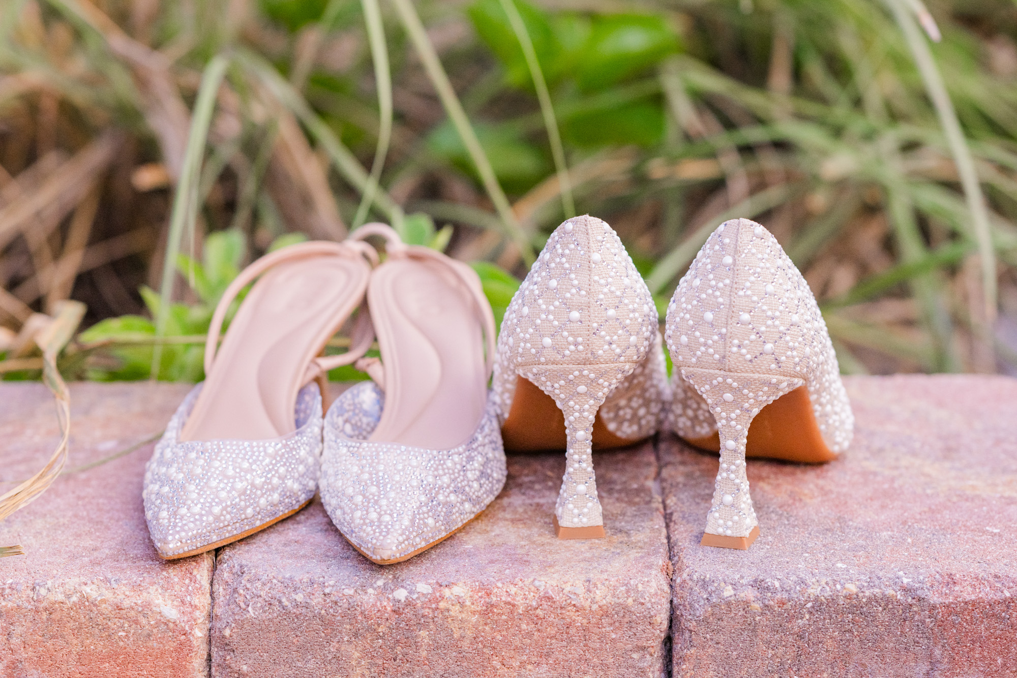 Pair of pearl-embellished wedding shoes photographed on a brick ledge.