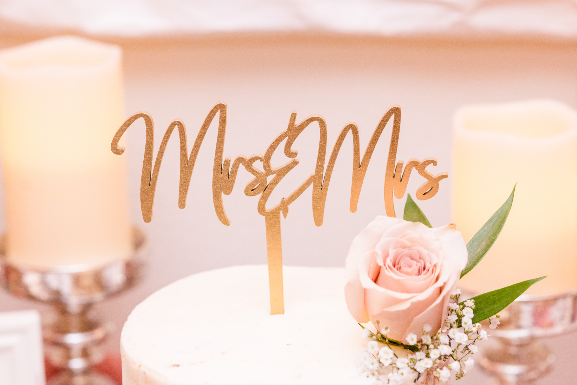 Wedding cake topped with a gold “Mrs & Mrs” sign and a blush rose.