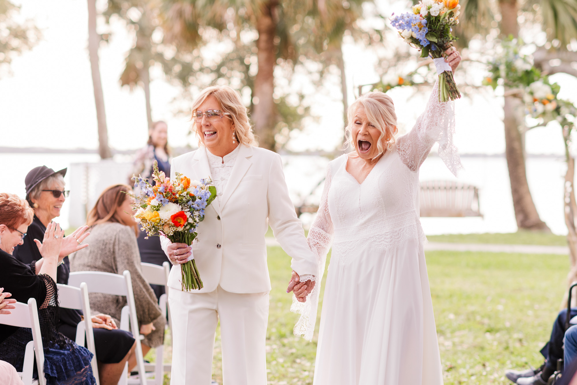 Newly married brides walking hand in hand down the aisle as guests applaud.