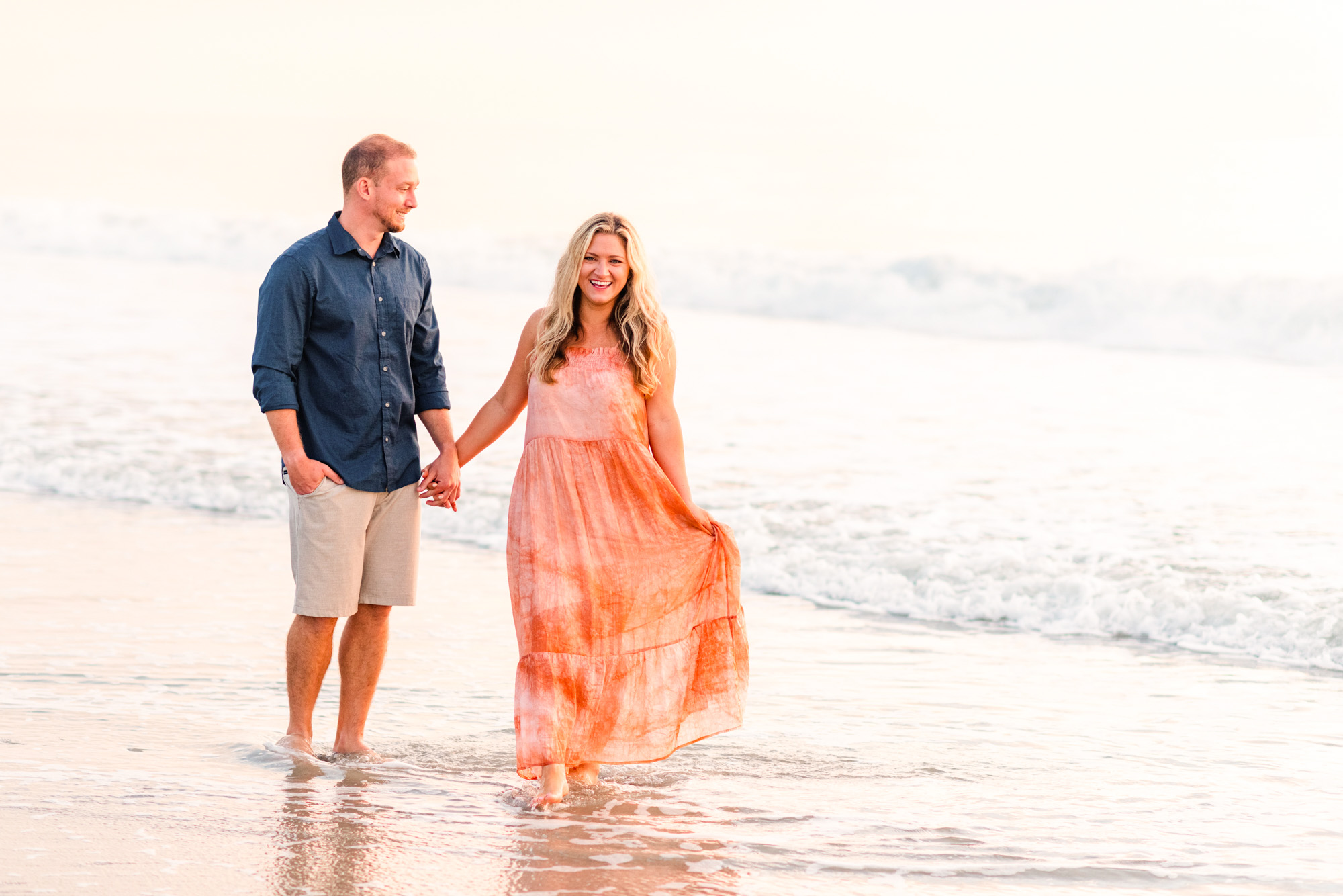 Man holding hand of girl wearing an orange dress during a sunrise engagement session