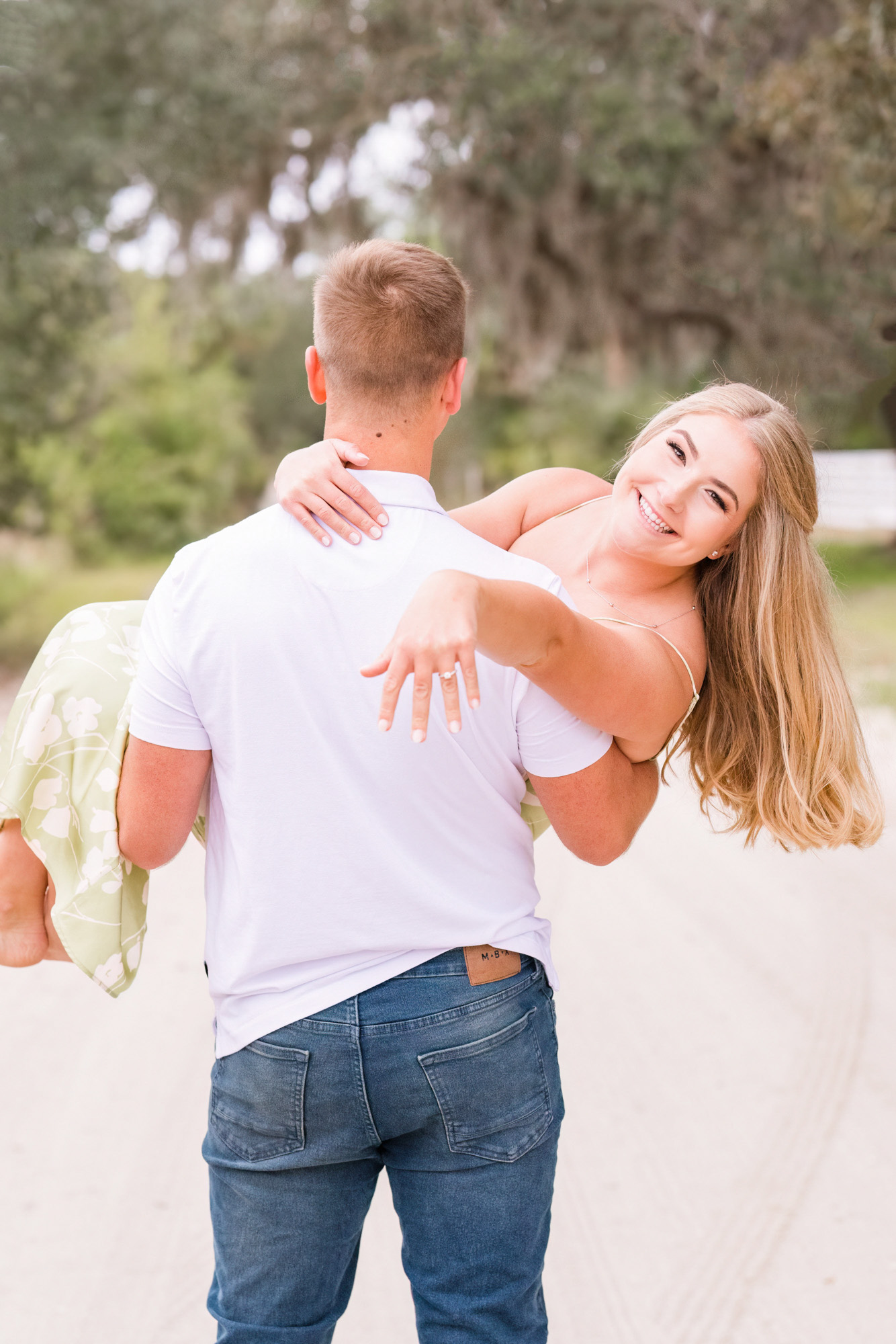 Man holding woman who is showing off her ring while on their engagement session on a dirt road