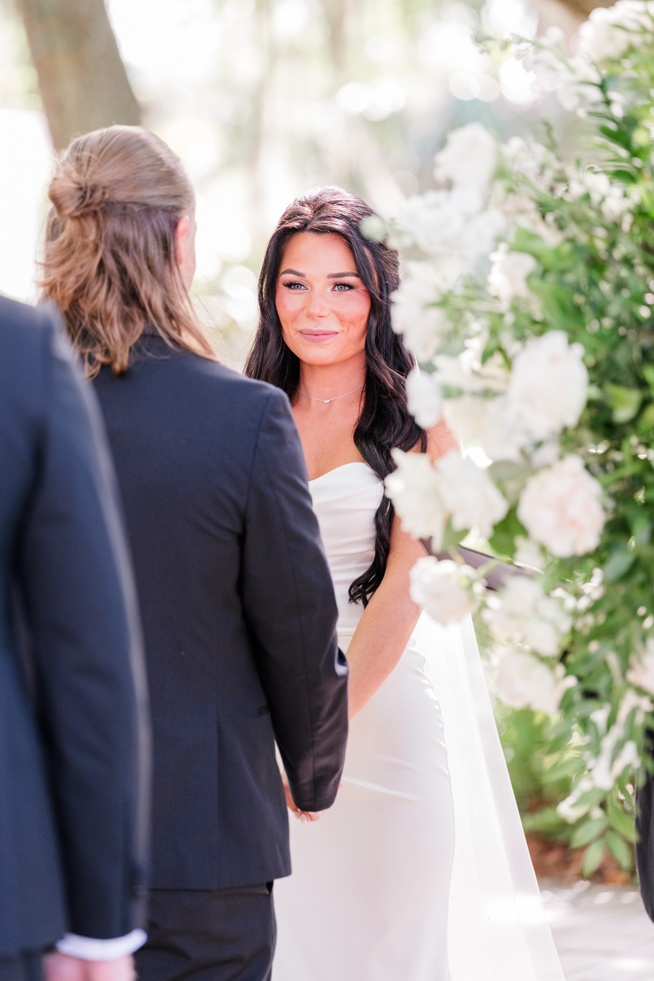 Bride looking at her partner during an outdoor wedding ceremony framed by white flowers.