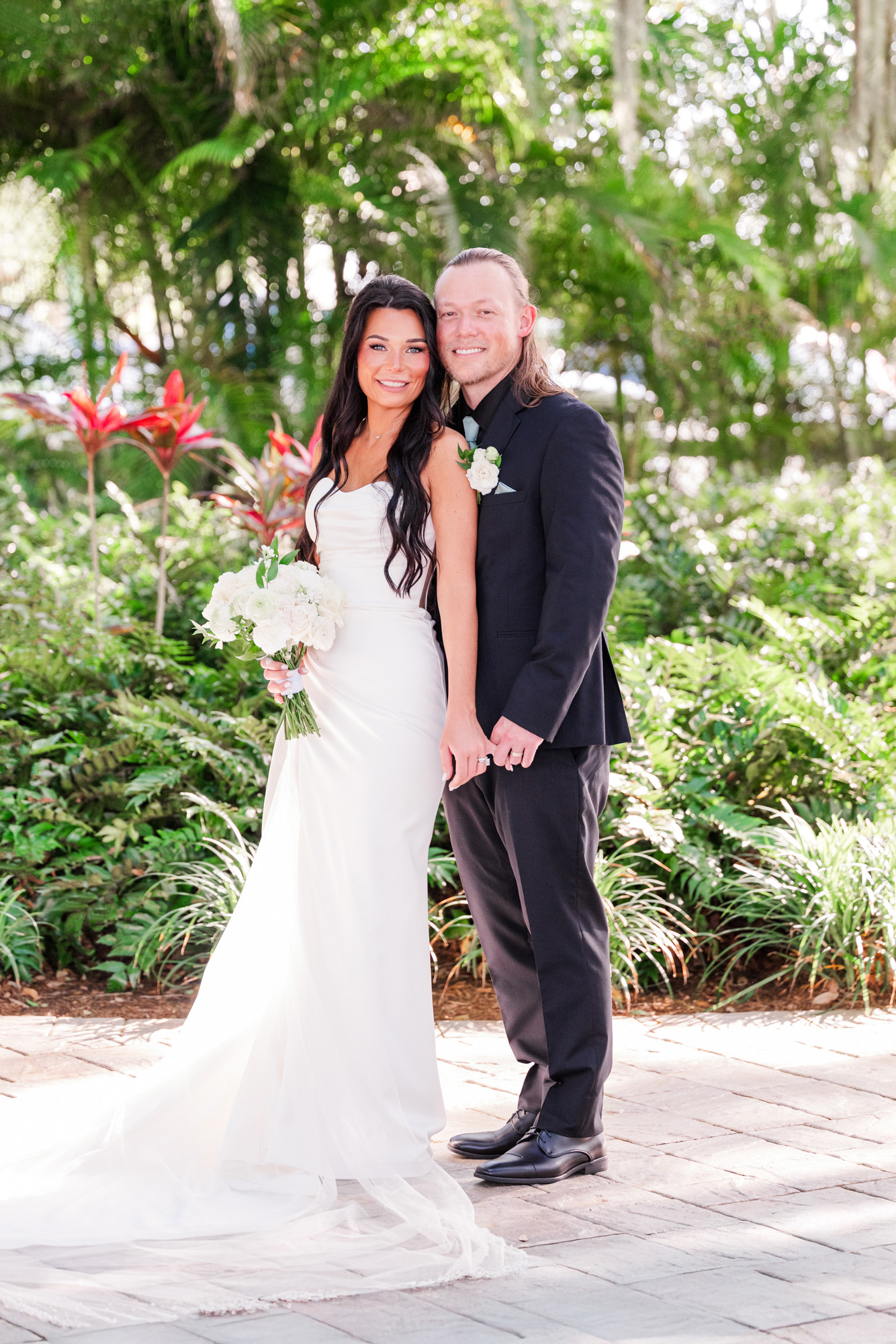 Bride and groom posing together in a lush garden after their wedding ceremony.