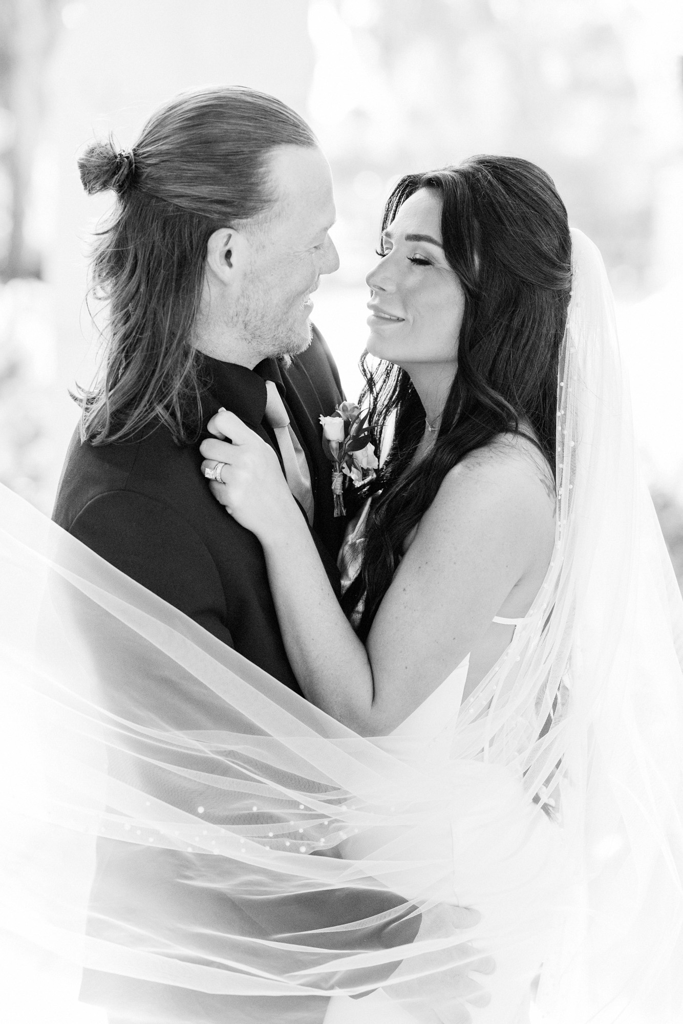 Black-and-white portrait of bride and groom standing close together beneath her flowing veil.