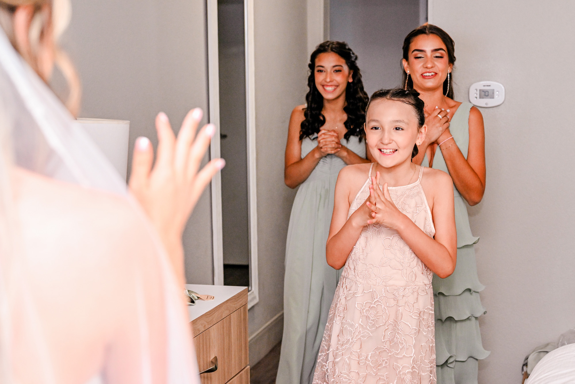 Flower girl smiling excitedly while bridesmaids react to seeing the bride in her dress.