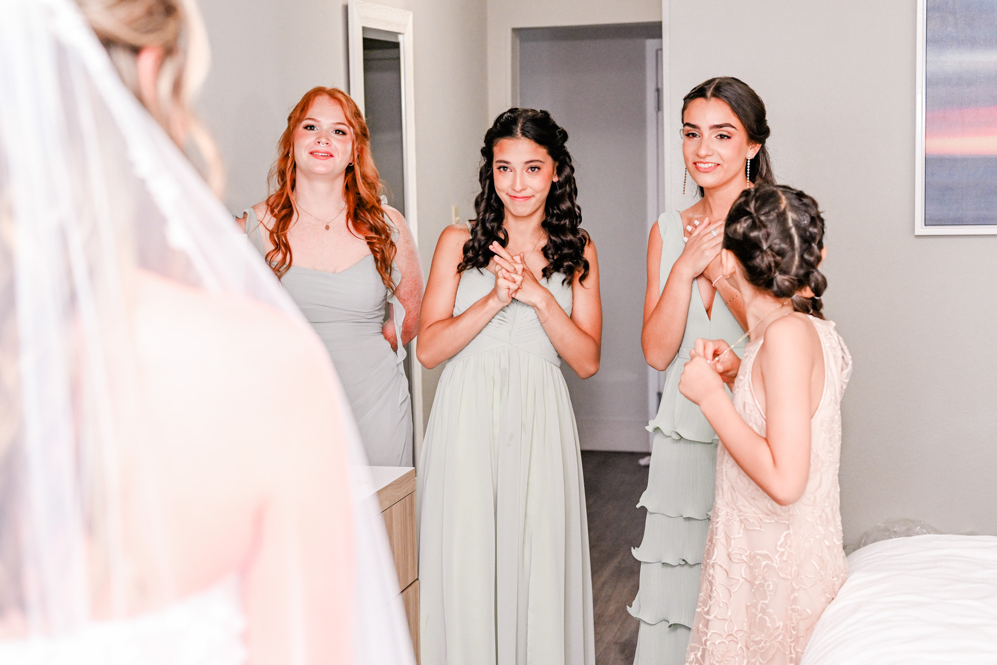 Bridesmaids smiling at the bride during a first-look moment in the getting-ready room.