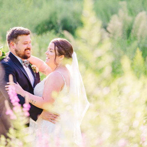 Bride and groom laughing together among wildflowers during golden-hour wedding portraits.
