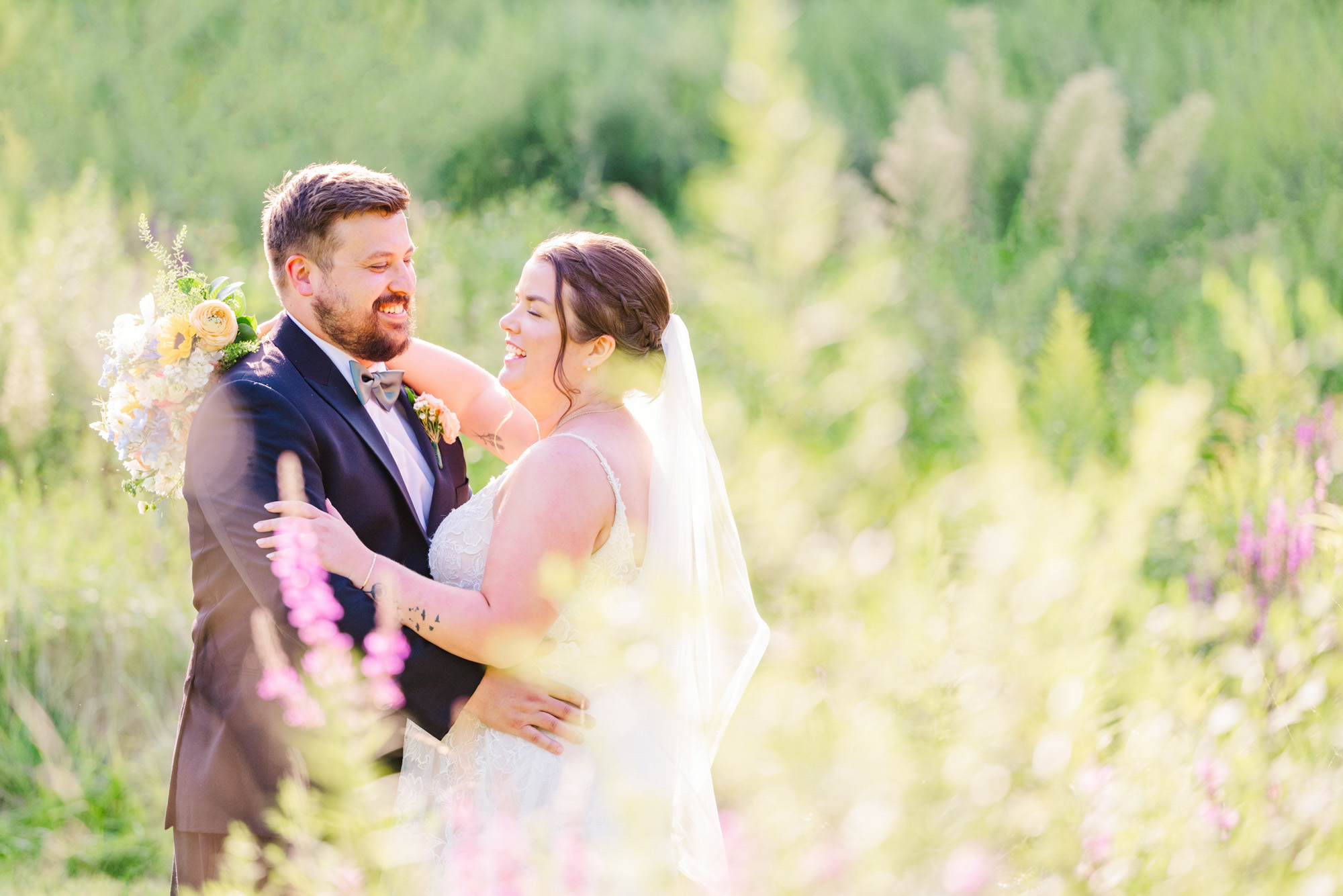 Bride and groom laughing together among wildflowers during golden-hour wedding portraits.