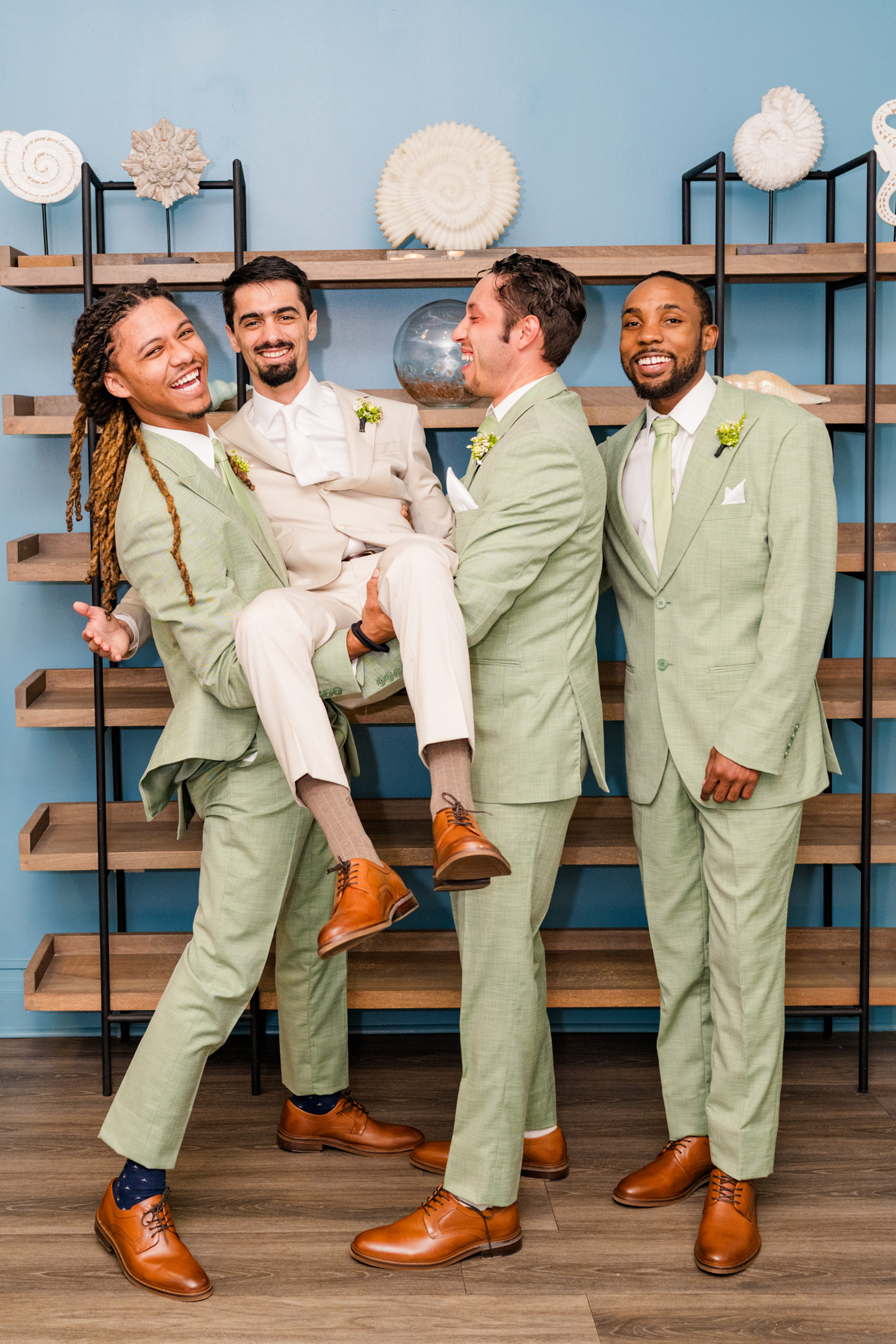 Groom being lifted by smiling groomsmen in matching sage green wedding suits.