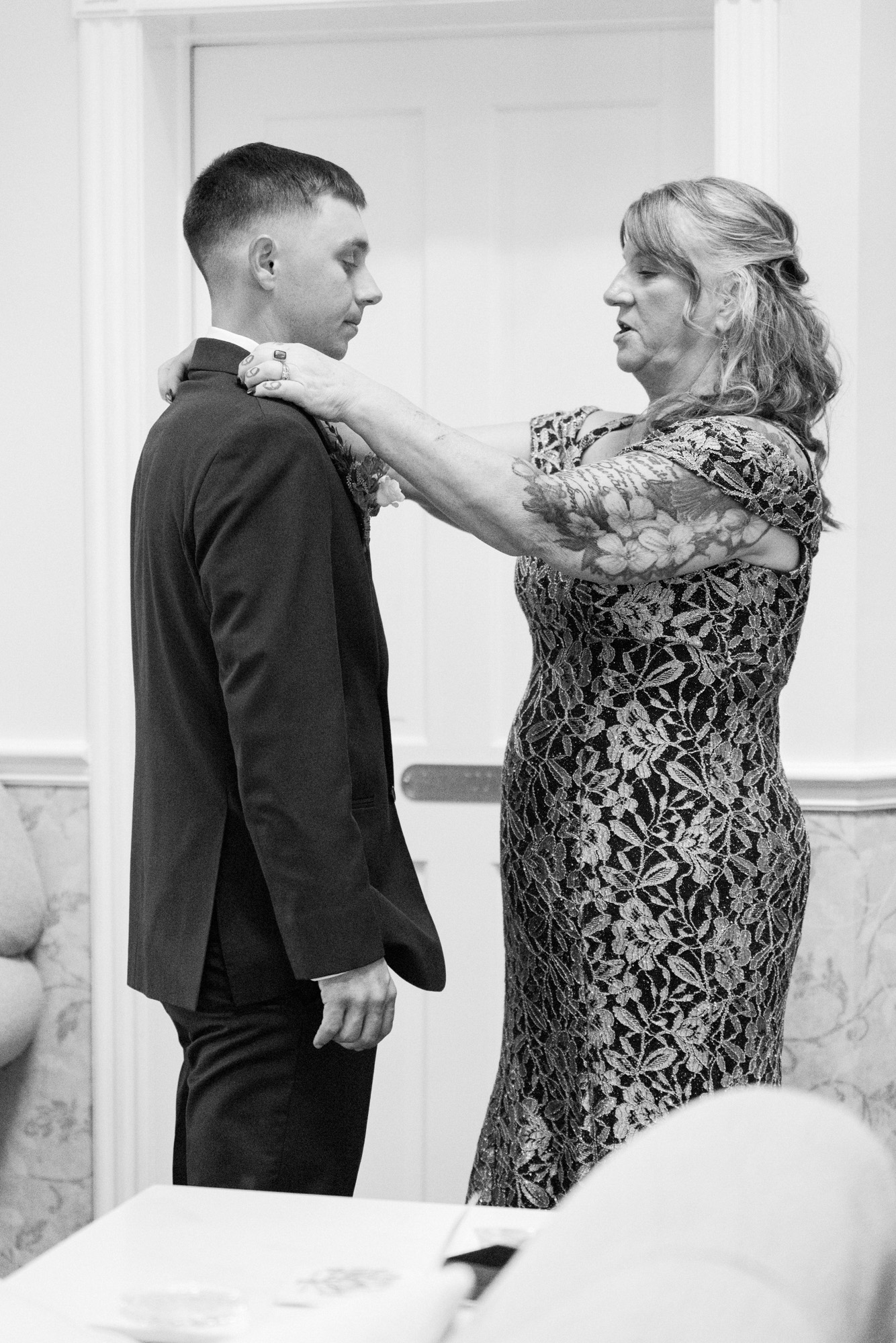 Woman adjusting a groom’s suit collar during wedding preparations.