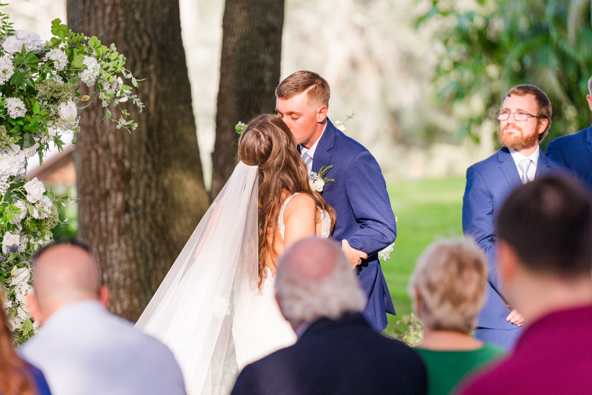 Bride and groom sharing their first kiss during an outdoor wedding ceremony.