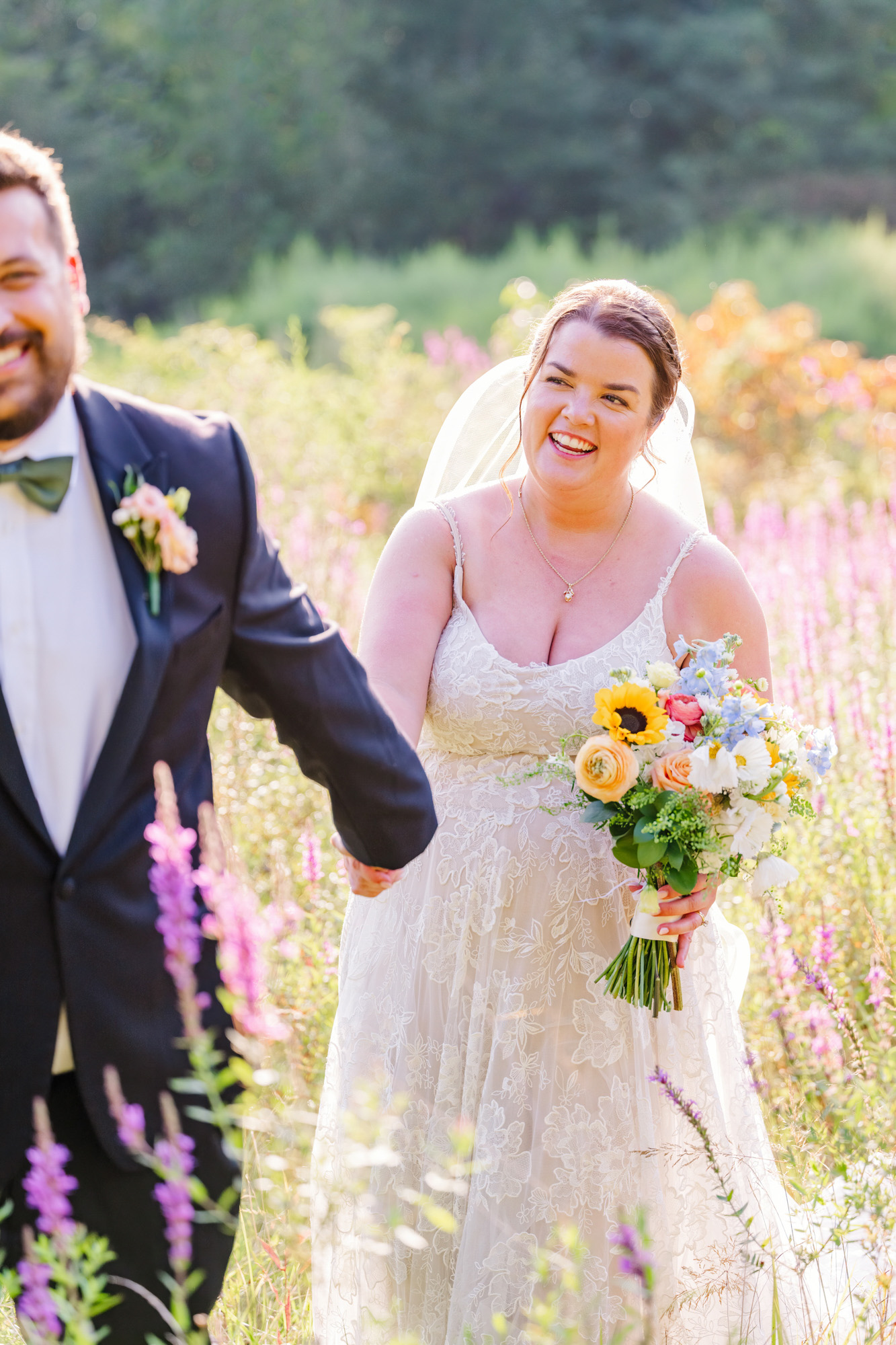 Bride smiling and laughing while holding a colorful bouquet in a field of wildflowers.