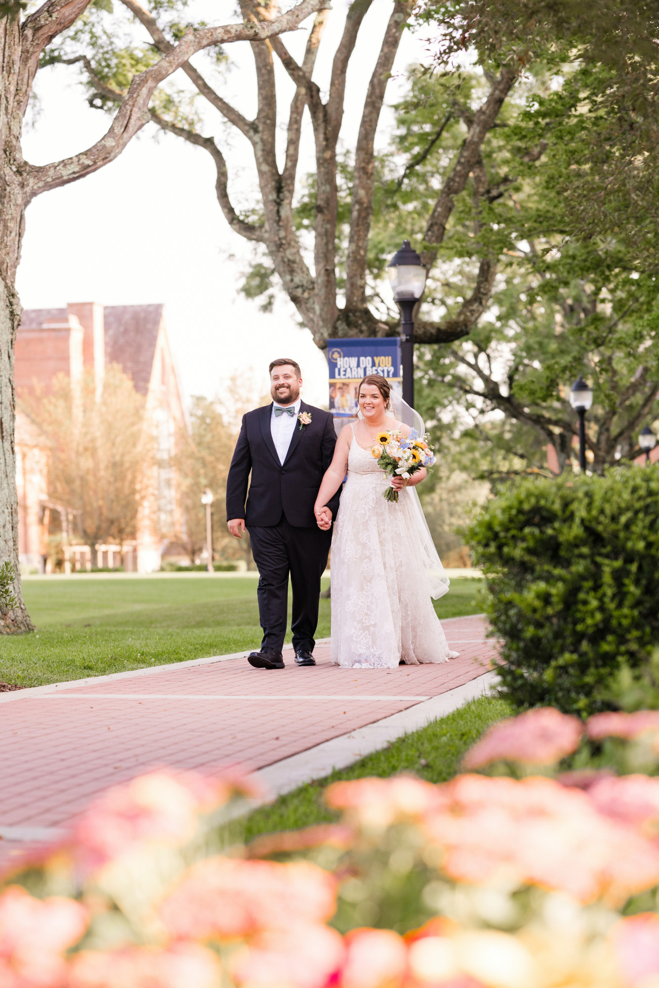 Bride and groom walking together beneath large trees at Trinity Pawling School.